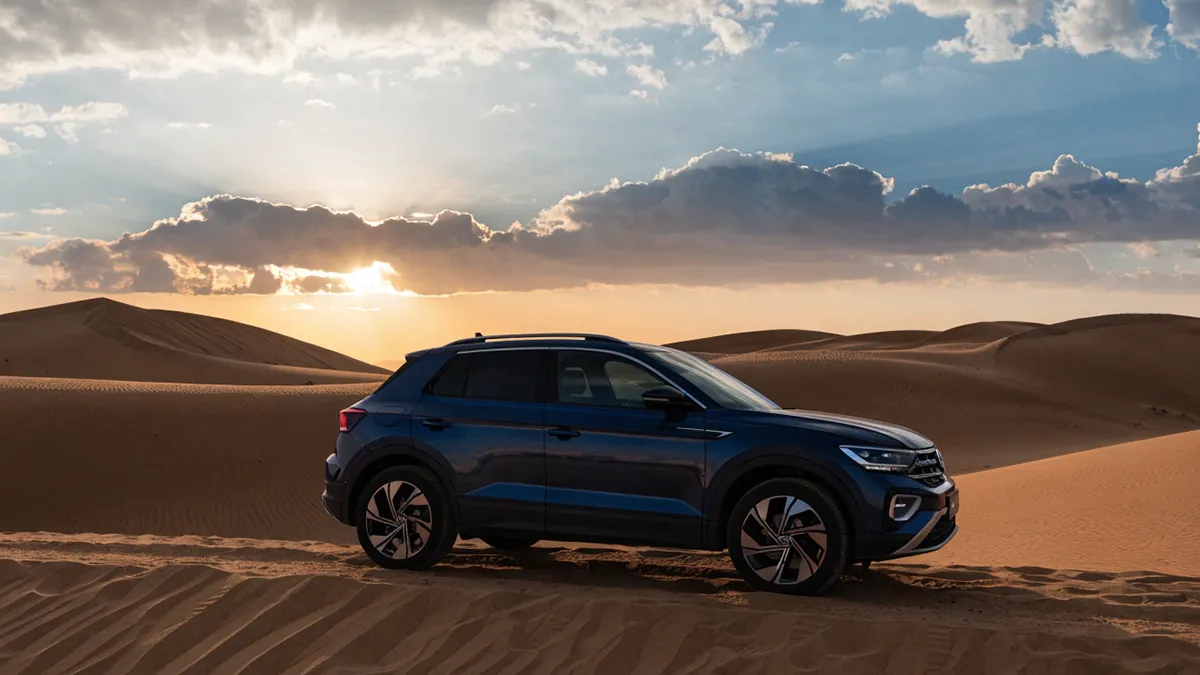 Vue frontale d’un Volkswagen T-roc 2024 stationné sur un terrain sablonneux au Maroc sous la lumière douce du lever du soleil, sans texte ni chiffres. T-roc