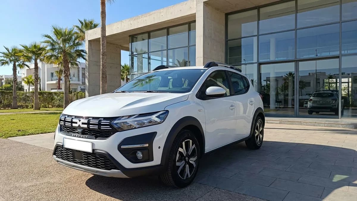 Dacia Sandero Stepway garée devant une agence de location à Agadir sous un ciel ensoleillé, palmiers en arrière-plan, sans texte dacia sandero Stepway