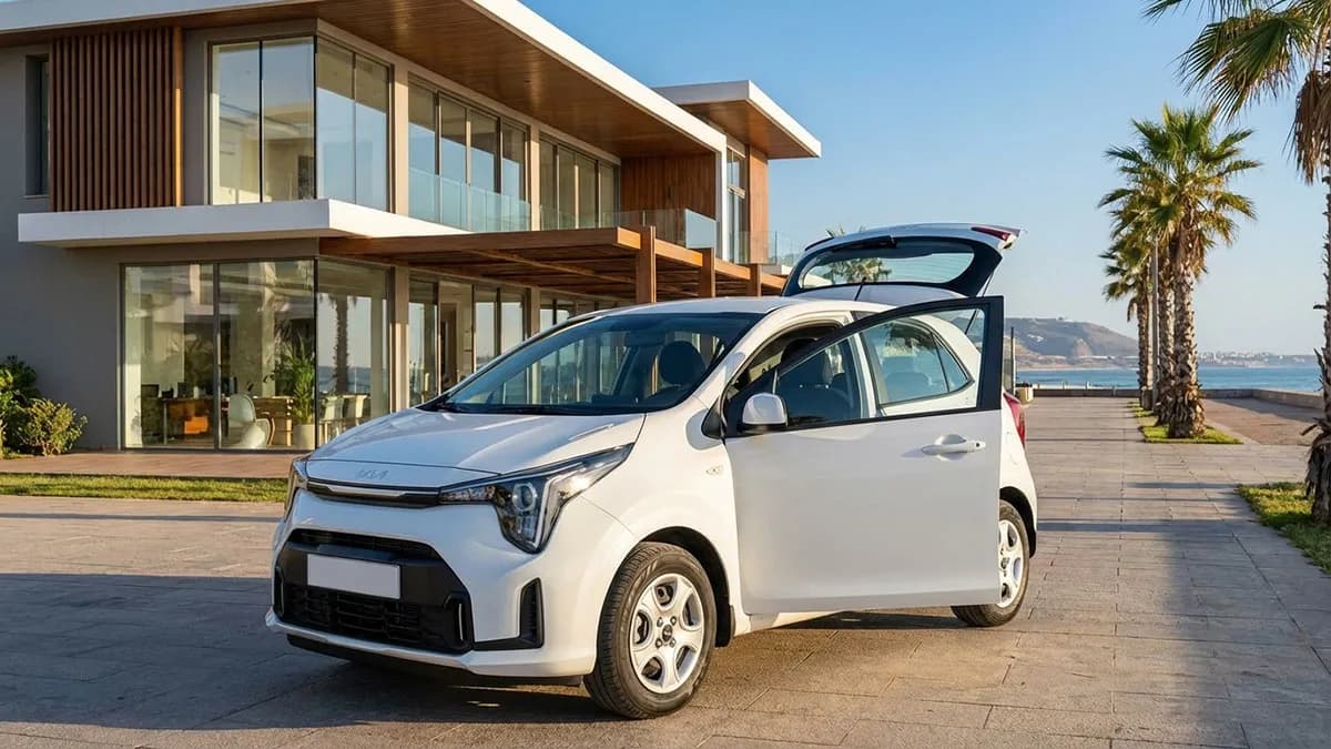 Kia Picanto 2025 rouge stationnée devant une agence de location à Agadir avec vue sur l’océan.