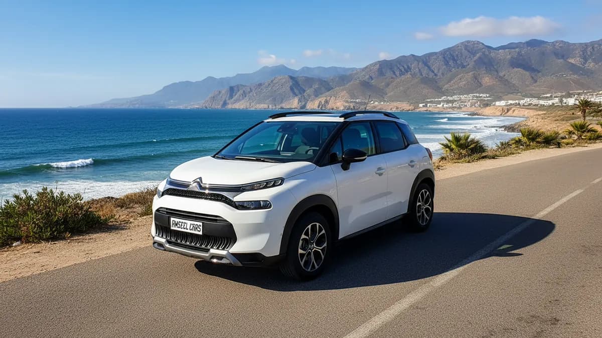Vue de profil d’une Citroën C3 Aircross blanche 2024 garée sur une route côtière marocaine avec l’océan Atlantique et des montagnes en arrière-plan