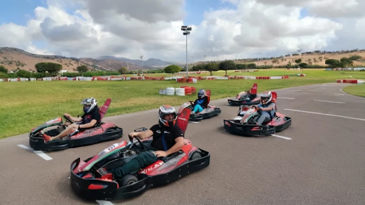 Un pilote de kart accélérant sur la piste avec des encadrants en arrière-plan souriant, mettant en avant l’atmosphère accueillante du Maroc Racing Karting Agadir.