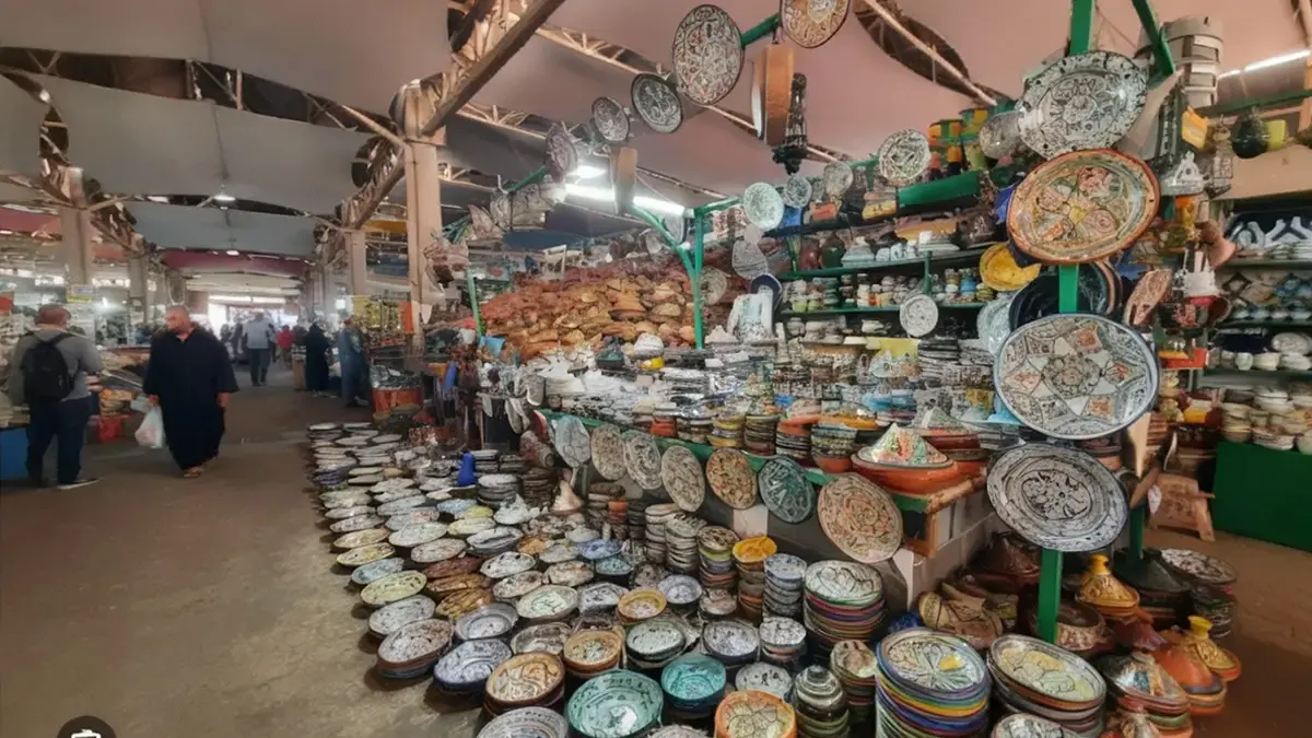 Allée du Souk El Had à Agadir avec étals de céramiques, tajines colorés et visiteurs, ambiance authentique et vivante du marché.