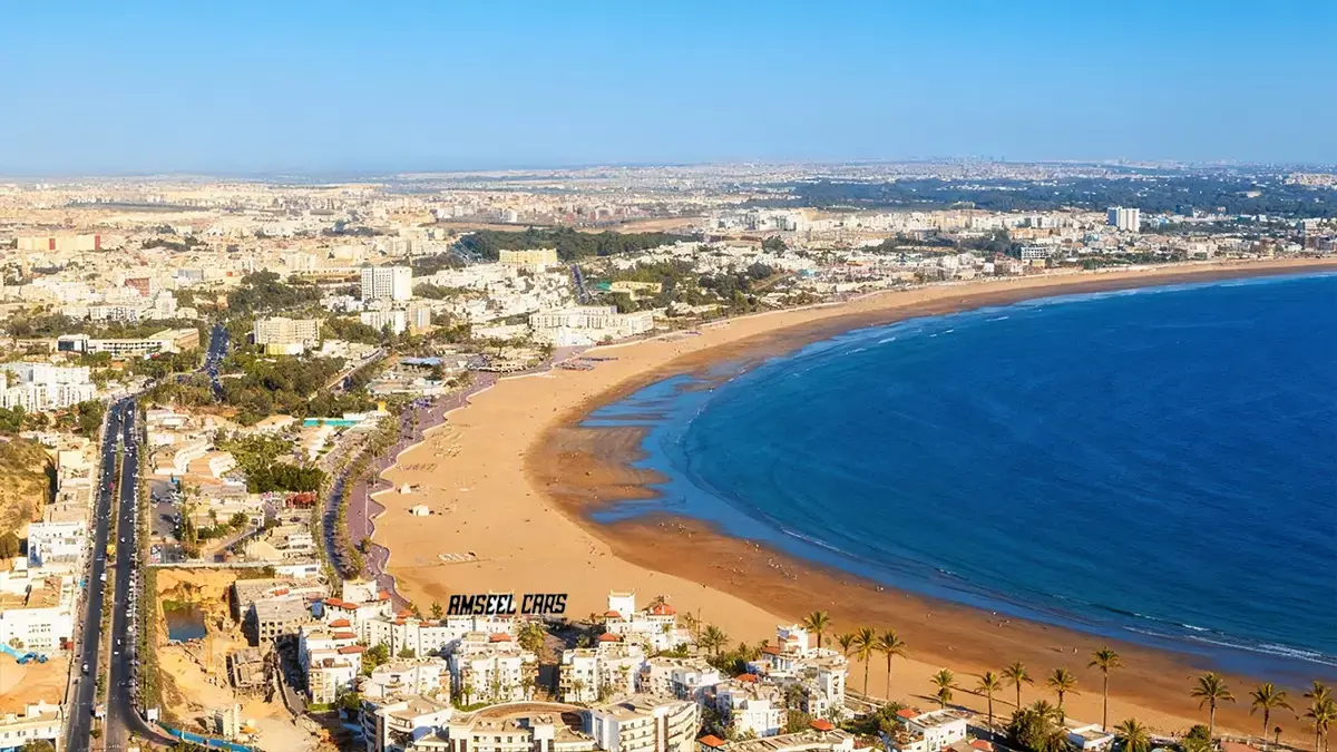 Panorama aérien d’Agadir au Maroc avec plage en arc, promenade bordée de palmiers et Atlantique d’un bleu profond